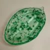 Un vide-poche en forme de feuille verte lumineuse posé sur une petite table en bois, rempli de quelques clés et pièces de monnaie.
