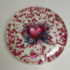 Vide-poche en résine époxy de forme ronde avec un cœur au centre, entouré de paillettes roses et de fleurs en résine, parfait pour ranger des petits objets.