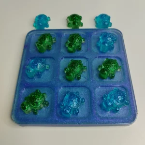 Jeu de morpion en résine époxy avec incrustations de paillettes bleues et violettes.