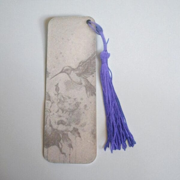 marque page oiseau qui butine-Photoroom (1) Marque-page en HDF gravé d'un colibri en vol, ficelle violette, tons beiges marbrés, design élégant.