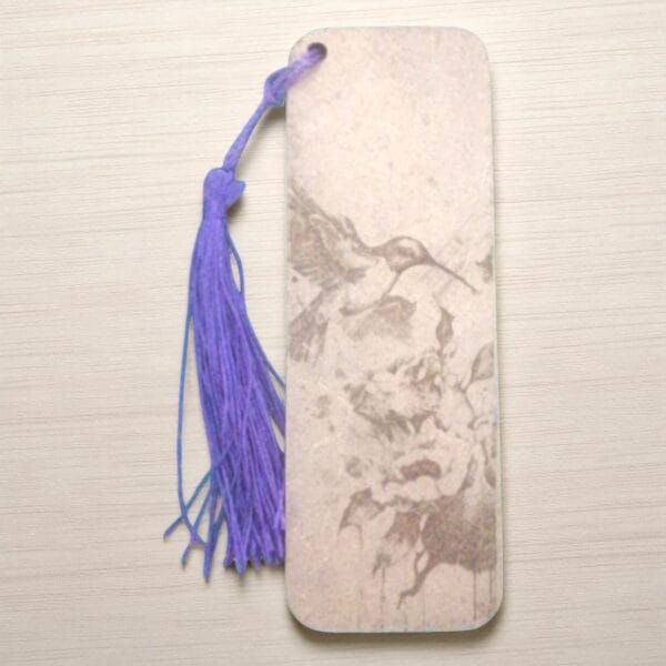 marque page oiseau qui butine-Photoroom (3) Marque-page en HDF gravé d'un colibri en vol, ficelle violette, tons beiges marbrés, design élégant.