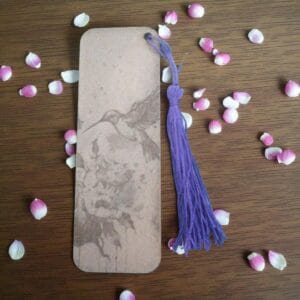 Marque-page en HDF gravé d'un colibri en vol, ficelle violette, tons beiges marbrés, design élégant.