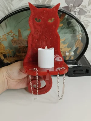 porte-bijoux-chat-resine-rouge-lumineux Un magnifique porte-bijoux chat en résine rouge translucide, éclairé de l'intérieur par une douce lumière, posé sur une table de chevet avec quelques bagues à sa base.