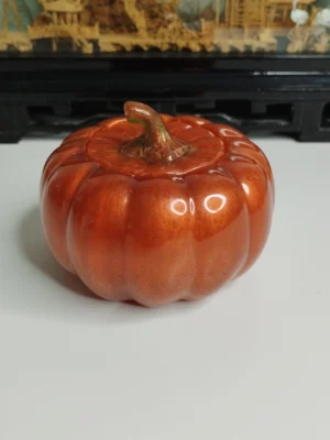 boite-citrouille-resine-halloween Une boîte décorative en résine brillante en forme de citrouille orange, posée sur une table en bois entourée de quelques feuilles d'automne séchées.