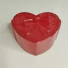 boite-bijoux-coeur-resine-rose Une magnifique boîte à bijoux en forme de cœur, de couleur rose nacré, posée sur une table en bois baignée de lumière naturelle.