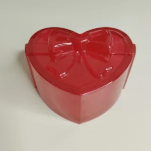 Une magnifique boîte à bijoux en forme de cœur, de couleur rose nacré, posée sur une table en bois baignée de lumière naturelle.