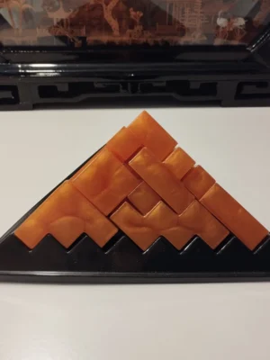 casse-tete-pyramide-resine-epoxy-orange Une vue de face de la pyramide assemblée, révélant le bel orange profond de la résine époxy contrasté par les lignes noires nettes des 23 pièces emboîtées.