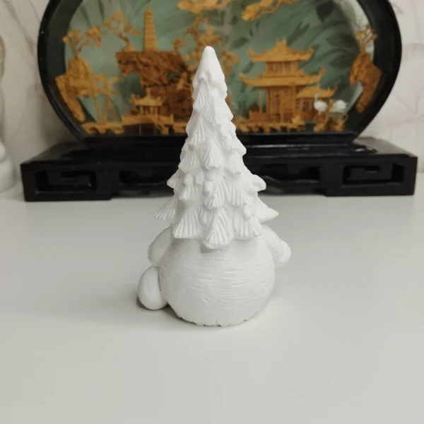 Gros plan sur le manteau finement texturé et le petit sapin de cette statuette de Noël artisanale.