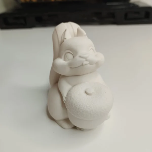 Une petite statuette écureuil en résine à peindre vue de face, montrant l'animal assis tenant un petit fruit rond.