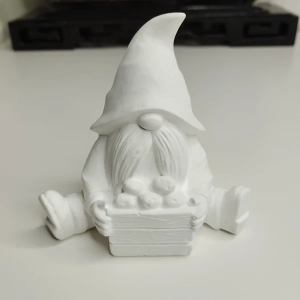 gnome-assis-resine-acrylique-blanc Notre gnome assis, vu de face, montrant son grand bonnet texturé et sa longue barbe, tenant tendrement son petit panier rempli de trois pommes.