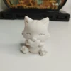 statuette-chat-assis-coeur-face Petite figurine d'un chat blanc assis tenant tendrement un cœur entre ses pattes avant, posée sur une table en bois clair.