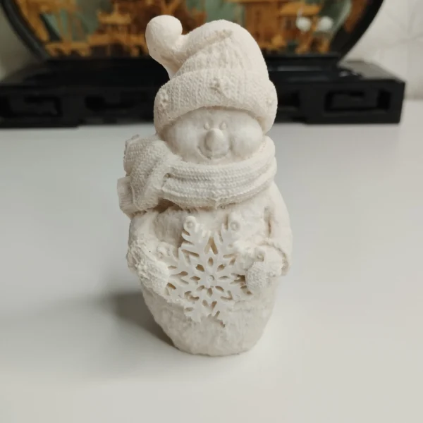 bonhomme-neige-resine-face-relief Figurine souriante de bonhomme de neige avec un bonnet tricoté et une écharpe, dévoilant un beau flocon de neige en relief sur le ventre, prête à être peinte.