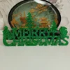 decoration-merry-christmas-resine-face Vue de face d'une décoration de Noël verte en résine, affichant l'inscription Merry Christmas avec des flocons et des sapins scintillants.