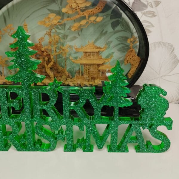 Gros plan sur les lettres ajourées et le renne stylisé de la décoration "Merry Christmas" en résine verte