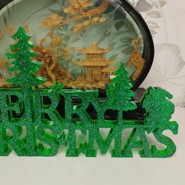 lettrage-vert-sapin-paillettes-details Gros plan sur la texture d'un lettrage merry christmas vert sapin, montrant les reflets irisés et la surface parfaitement lisse de la matière.