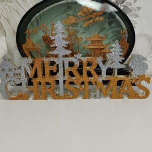 Panneau "Merry Christmas" en résine époxy pailletée posé sur une étagère, entouré de bougies.