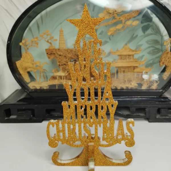 Décoration de table noël en résine pailletée dorée avec l'inscription We Wish You a Merry Christmas, délicatement posée sur une cheminée festive.