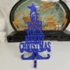 Lettres joyeux noël à poser d'une hauteur de 175 mm, en résine bleu vif scintillante, entourées de branches de sapin et de petites pommes de pin.