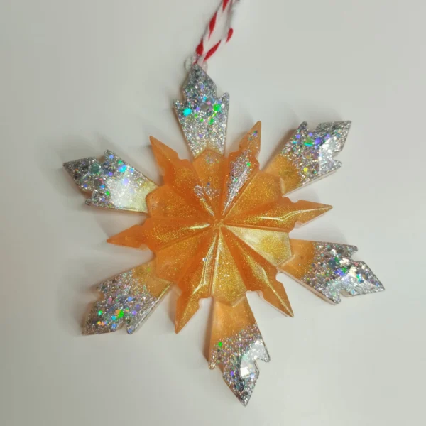 detail-artisanat-flocon-dore Gros plan sur les finitions d'un ornement flocon de neige scintillant, montrant le dégradé ambré de la résine lisse et la densité des paillettes irisées sur les extrémités.