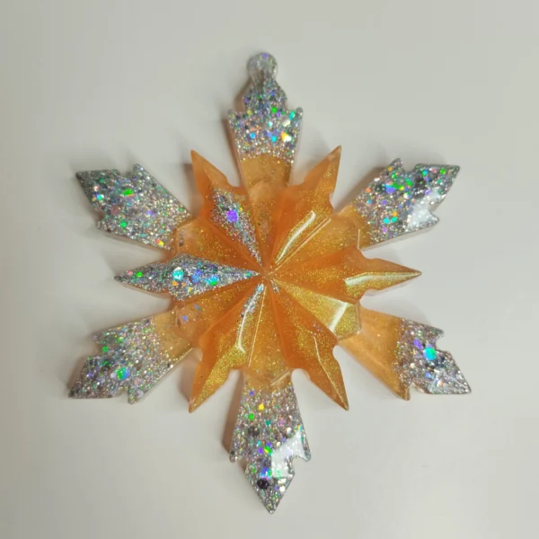 ornement-flocon-geometrique-resine Une décoration de noël flocon en résine posée sur une table en bois, laissant apparaître ses reflets dorés et ses pointes scintillantes à la lumière du jour.