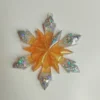 suspension-sapin-paillettes-argent Une suspension flocon géométrique pour sapin accrochée à une branche de conifère, captant les lueurs chaudes des guirlandes environnantes.