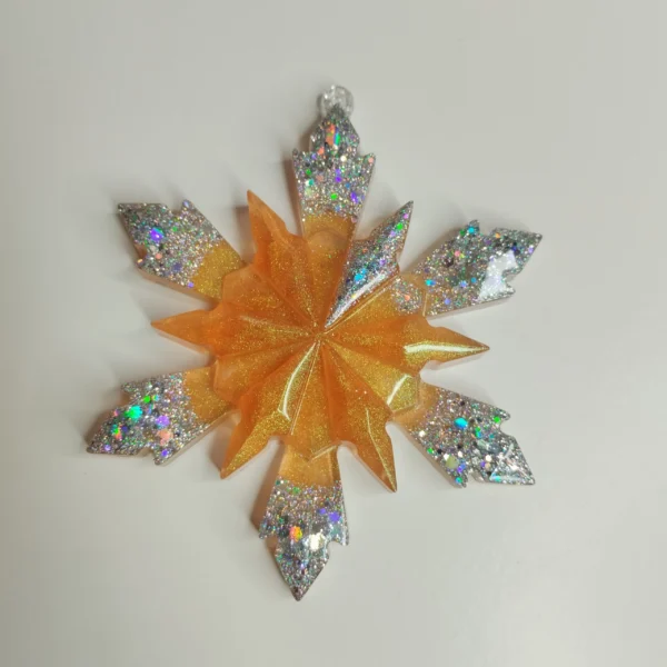 suspension-sapin-paillettes-argent Une suspension flocon géométrique pour sapin accrochée à une branche de conifère, captant les lueurs chaudes des guirlandes environnantes.