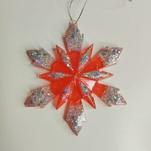 Ornement flocon de neige rouge pailleté en résine époxy suspendu sur un sapin de Noël décoré