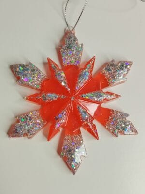 Ornement flocon de neige rouge pailleté en résine époxy suspendu sur un sapin de Noël décoré