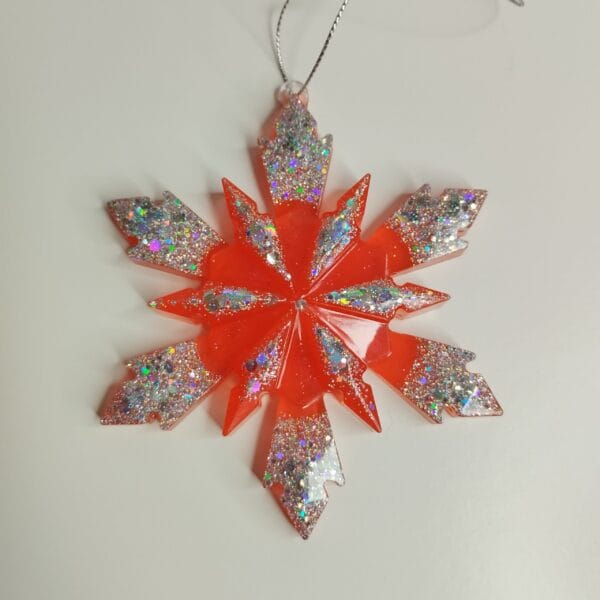 Ornement flocon de neige rouge pailleté en résine époxy suspendu sur un sapin de Noël décoré