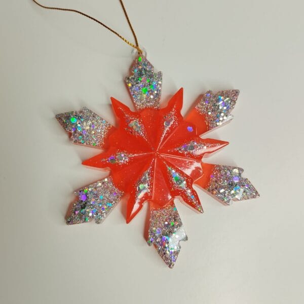 Flocon de neige rouge translucide posé sur une cheminée avec des guirlandes lumineuses dorées