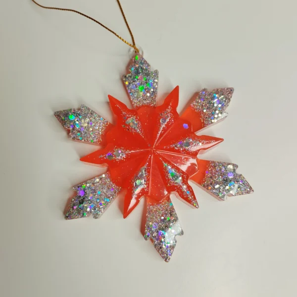 Flocon de neige rouge translucide posé sur une cheminée avec des guirlandes lumineuses dorées
