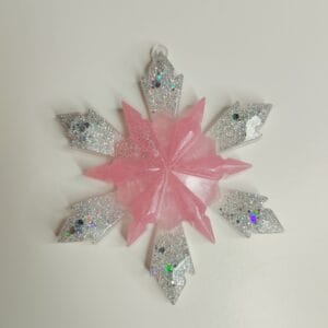 Ornement flocon de neige rose poudré en résine époxy suspendu sur un sapin de Noël décoré