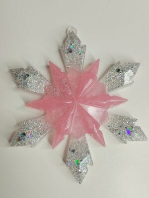 Ornement flocon de neige rose poudré en résine époxy suspendu sur un sapin de Noël décoré