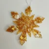 Un grand flocon à huit branches transparent rempli de paillettes dorées, suspendu délicatement à une branche de sapin de Noël.