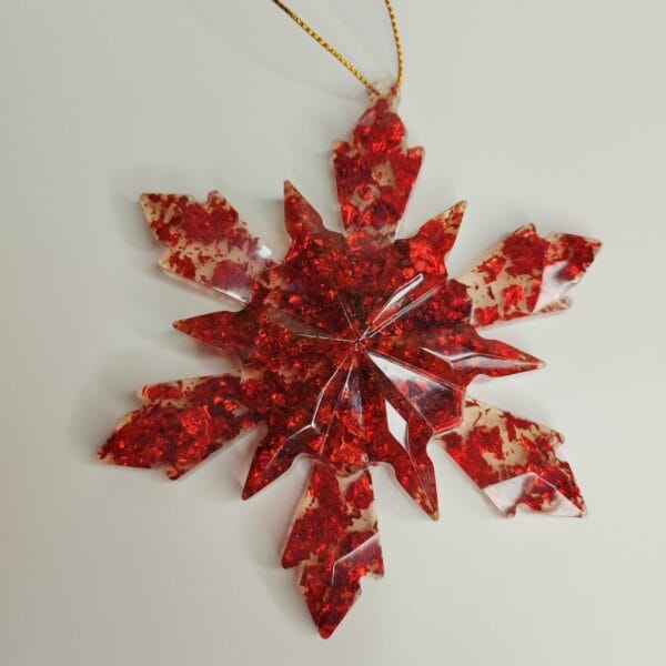 Flocon de neige rouge en résine posé sur une table avec des bougies et des guirlandes