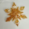 Gros plan sur les fragments métallisés brillants capturés dans la résine transparente de cette décoration de sapin flocon doré en résine.