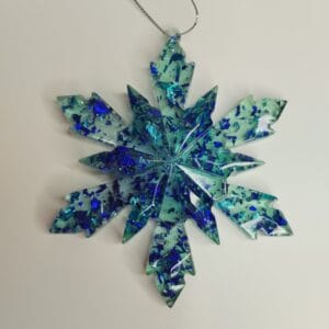 Flocon de neige turquoise et bleu nuit posé sur une étagère avec des guirlandes lumineuses bleues