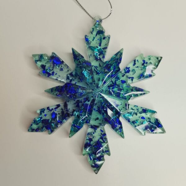Flocon de neige turquoise et bleu nuit posé sur une étagère avec des guirlandes lumineuses bleues
