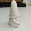 gnome-porte-sapin-details-sculpture Gros plan sur les mains du lutin tenant le mini sapin conique. On y voit clairement les détails lisses de la résine acrylique blanche et les jolis plis sculptés de son manteau d'hiver.