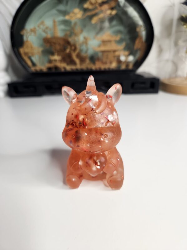 Figurine licorne assise en résine rouge profond avec inclusions de feuilles métalliques brillantes.