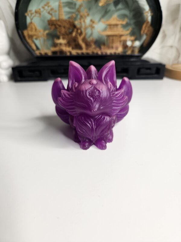 Statuette kitsune violette translucide en résine époxy exposée à la lumière du jour.