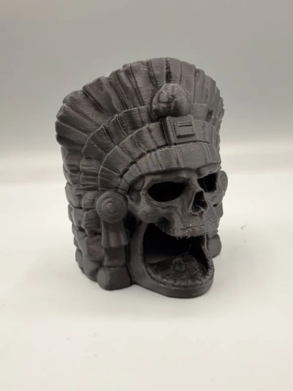 Cachette crâne aztèque pour terrarium installée au milieu de plantes verdoyantes et de substrat, créant un abri naturel et mystique pour les animaux.