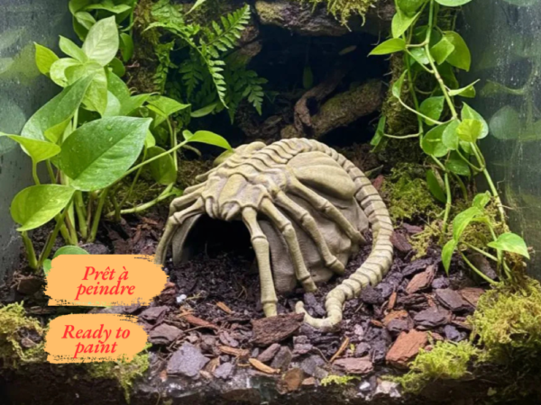 cachette-terrarium-facehugger-pla Vue de face d'une cachette pour terrarium en forme de roche, surmontée d'un parasite extraterrestre avec de longues pattes osseuses.