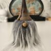 Un adorable gnome décoratif en bois tourné, posé sur une surface plane. On distingue parfaitement son grand chapeau sombre, son petit nez rond en bois clair et sa longue barbe grise qui tombe souplement.