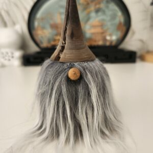 Un adorable gnome décoratif en bois tourné, posé sur une surface plane. On distingue parfaitement son grand chapeau sombre, son petit nez rond en bois clair et sa longue barbe grise qui tombe souplement.
