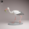 Figurine de cigogne blanche à peindre, debout sur un sol sableux, tenant fermement un lézard vert dans son long bec, montrant une posture de chasse dynamique.
