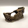Gros plan sur la partie arrière d'une cachette originale pour reptile, illustrant une cabine avec de petites fenêtres et un motif de tête de mort croisée de tibias gravé dans le faux bois.