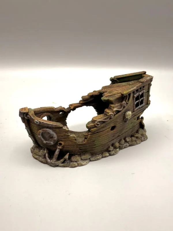 Gros plan sur la partie arrière d'une cachette originale pour reptile, illustrant une cabine avec de petites fenêtres et un motif de tête de mort croisée de tibias gravé dans le faux bois.